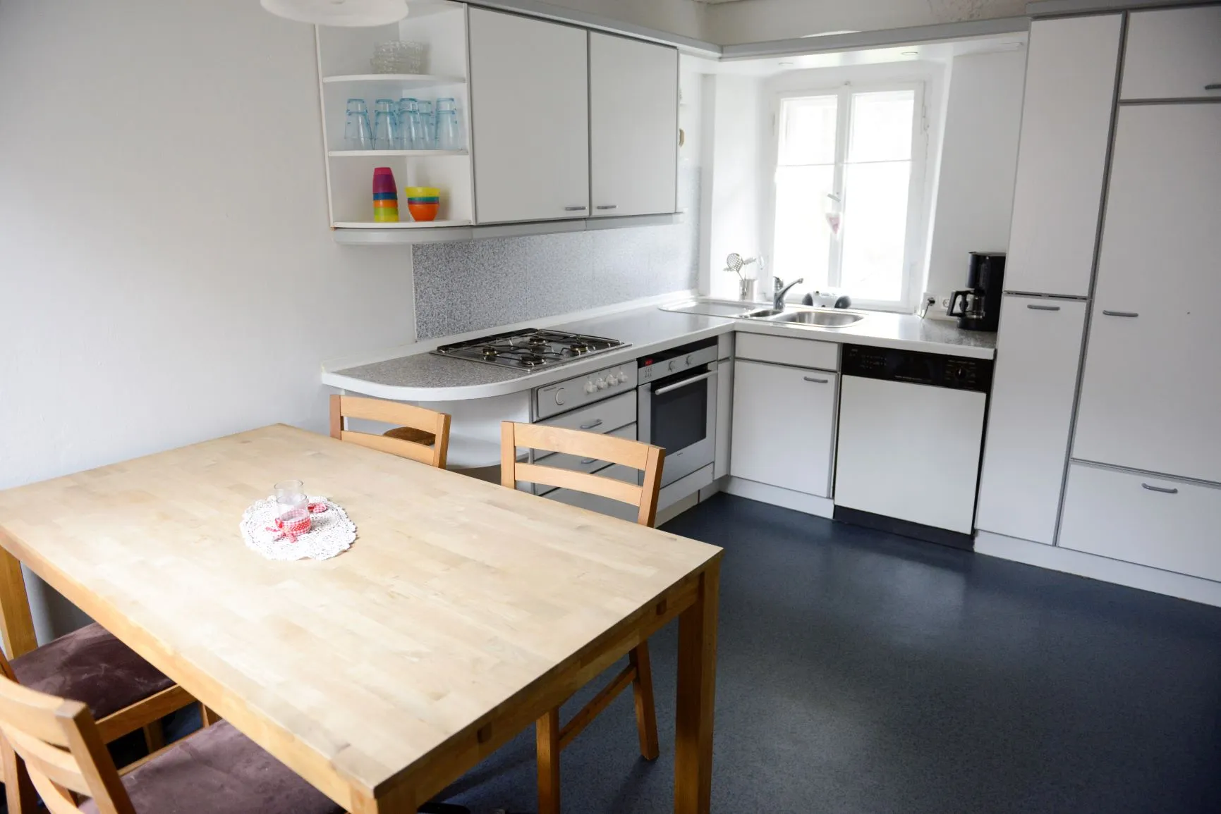 Die Einbauküche mit Gasherd, Backofen, Geschirrspüler, Kühlschrank und Kaffeemaschine, dazu ein großer Esstisch mit Stühlen.