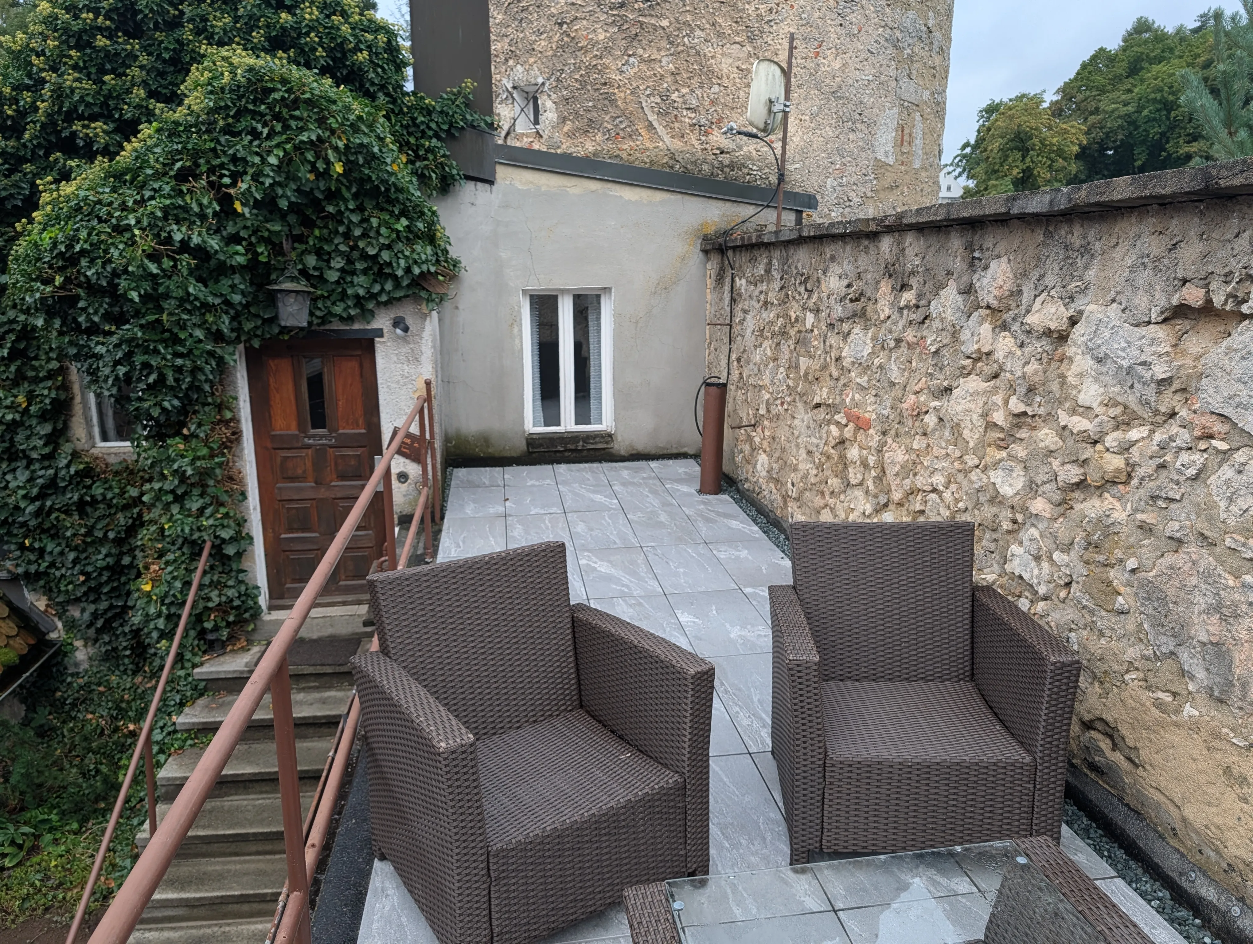 Die Terrasse am Fuß des Turms: Sessel und Glastisch, dahinter die Tür zur Wohnung und das Bruchsteinmauerwerk des Turms.