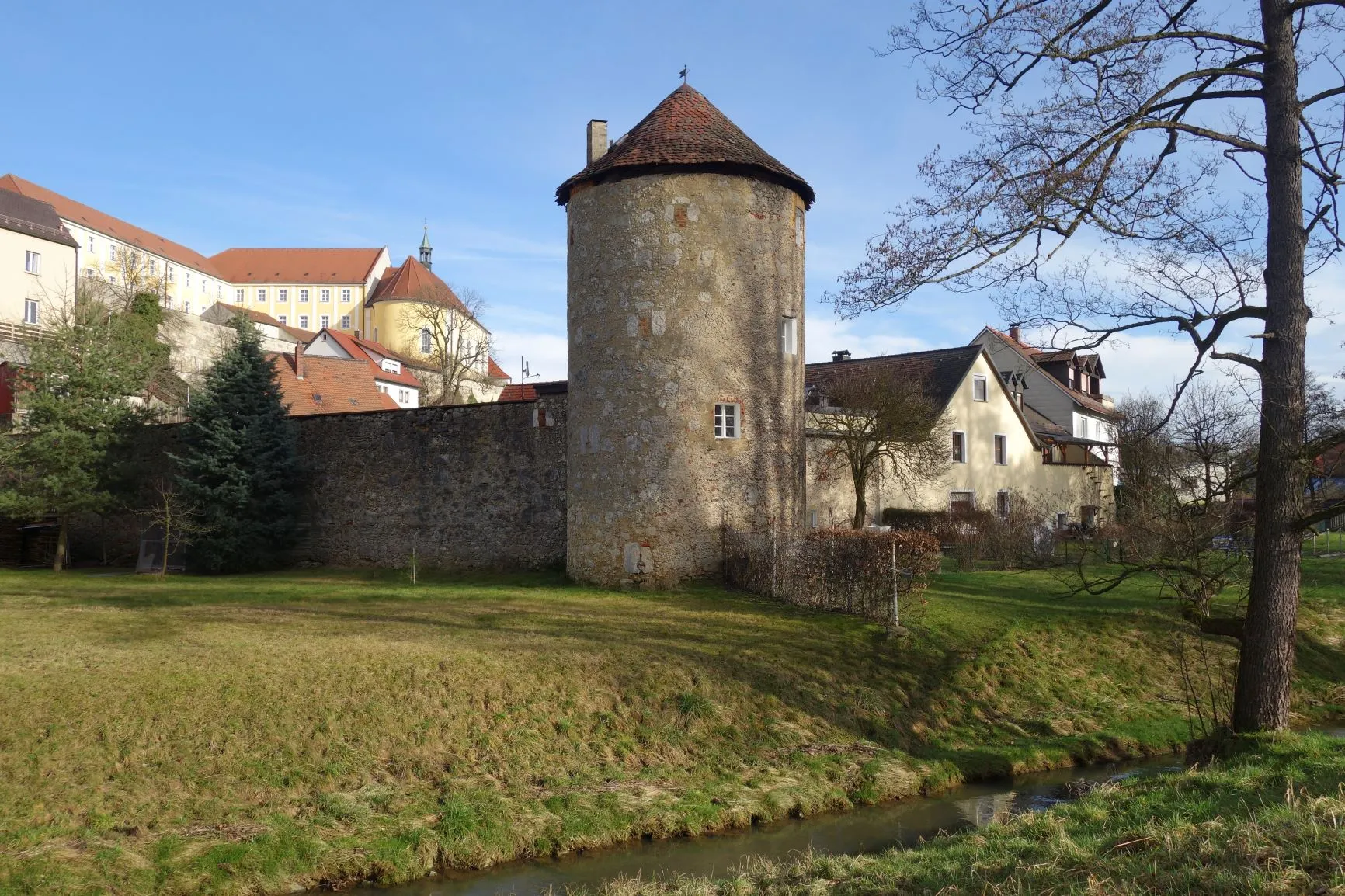Der Pulverturm in Sulzbach-Rosenberg: ein runder Bruchsteinturm mit Ziegeldach an der alten Stadtmauer, dahinter der Schlossberg.